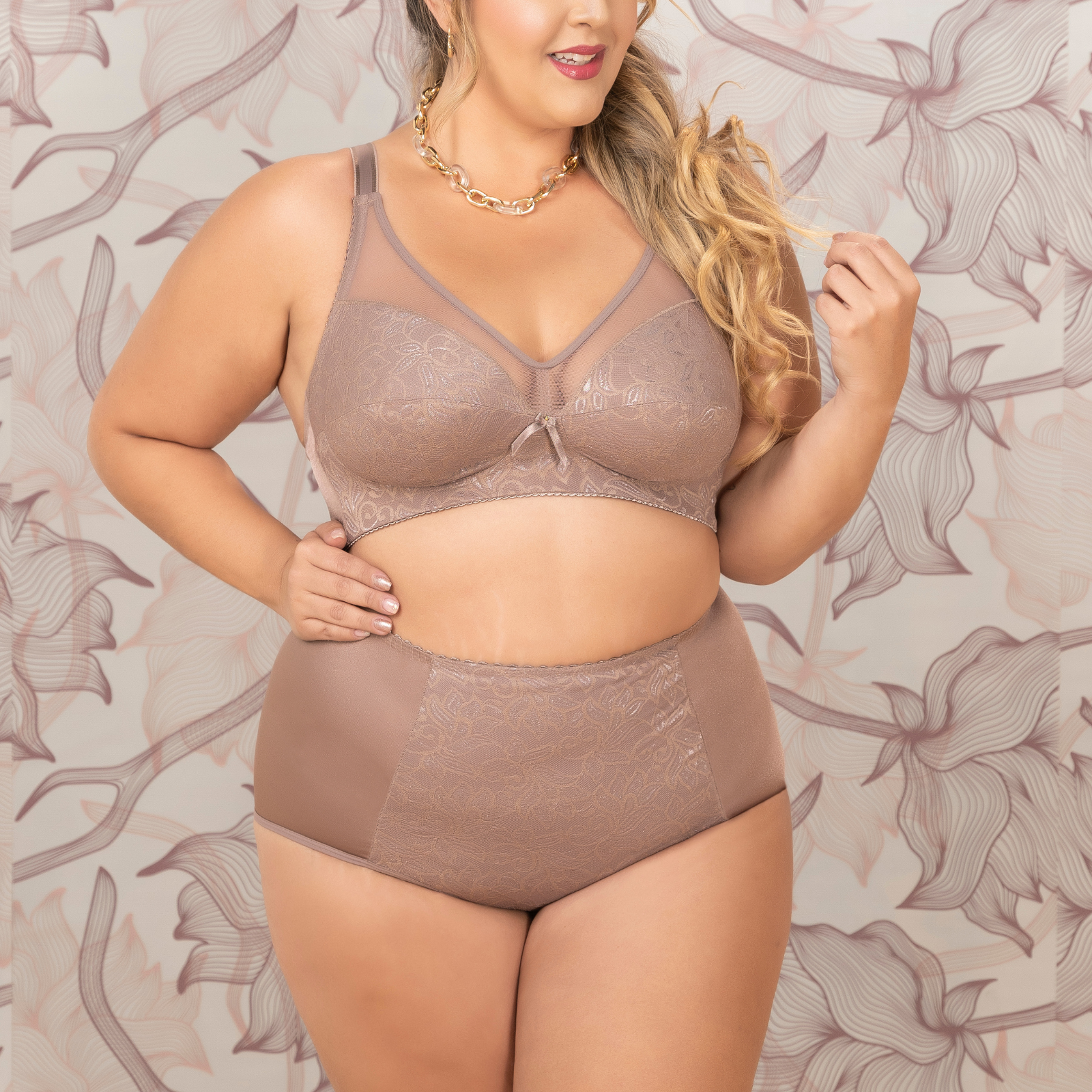 Woman wearing a brown lingerie set against a floral patterned wall.