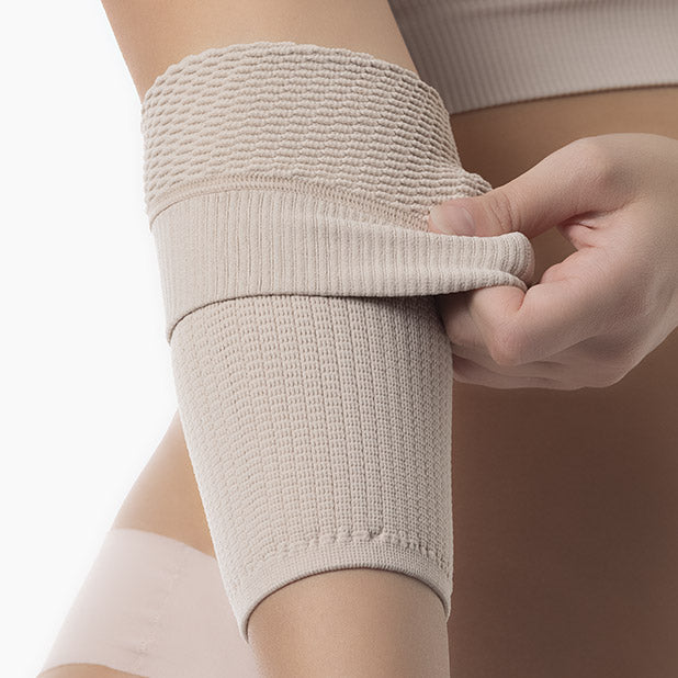 Person applying a beige compression bandage on their arm against a neutral background