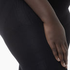 Close-up of a person wearing a black textured outfit with a hand resting on the hip.
